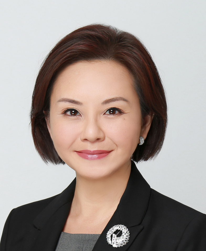 Person in black blazer and grey shirt, wearing a decorative floral brooch.